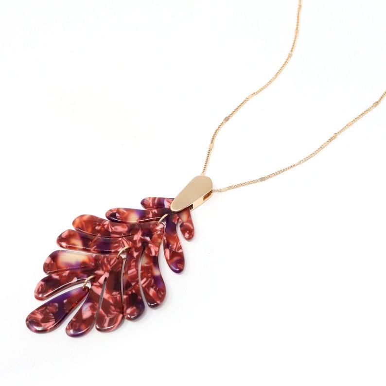 May include: A gold chain necklace with a large, red and purple leaf-shaped pendant. The pendant is made of a marbled material.