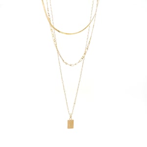 A set of triple layered necklace in gold with a small brush textured rectangle charm.