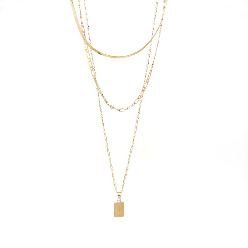 A set of triple layered necklace in gold with a small brush textured rectangle charm.