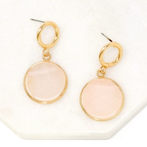 May include: Gold hoop earrings with a dangling pink circle pendant. The earrings have a simple, elegant design.