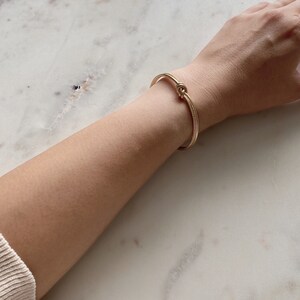 Arm wearing the textured gold knot cuff bracelet, resting on a white marble surface.