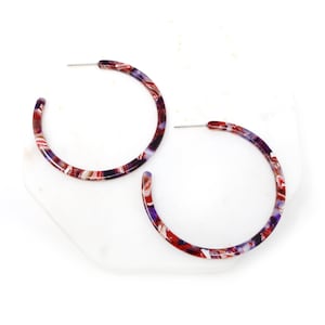 May include: A pair of large hoop earrings with a red, white, and purple marbled pattern.