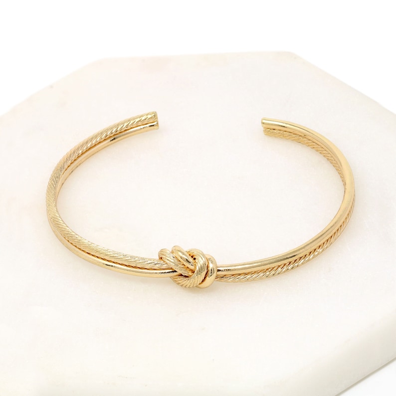 Textured gold rope knot cuff bracelet on a white marble tile.