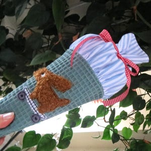 Könnte beinhalten: Ein blaugestreifter Stoffkegel mit einem braunen Hasen, der auf einem Spielzeug-Skateboard fährt. Der Kegel hat ein rot-weißes Karoband.