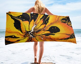 Puede incluir: Una toalla de playa con un diseño abstracto colorido con remolinos de amarillo, naranja y negro. La toalla está siendo sostenida por una persona en una playa.