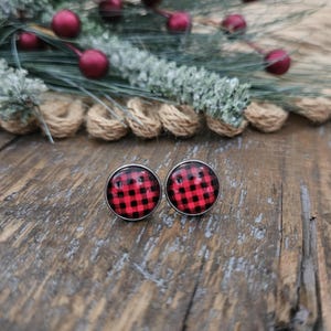 May include: A pair of red and black plaid stud earrings. The earrings are round and have a silver backing.