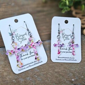 May include: A pair of floral cross earrings with silver hooks. The earrings are on a white card with the text "Blessed Stitch" and "Thank You for your purchase".