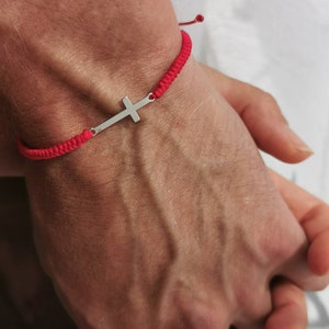 Puede incluir: Un brazalete de cuerda roja con un dije de cruz de plata.