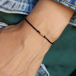 Op de afbeelding: Een eenvoudige zwarte armband met drie kleine gouden kralen.
