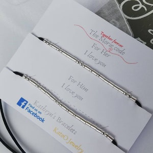May include: Two black cord bracelets with silver beads spelling out "I love you" in Morse code. The bracelets are displayed on a white card with the text "Together forever. The Morse code. For Her. I love you. For Him. I love you. Kathryn's Bracelets. Find us on Facebook. Katoo Jewelry."