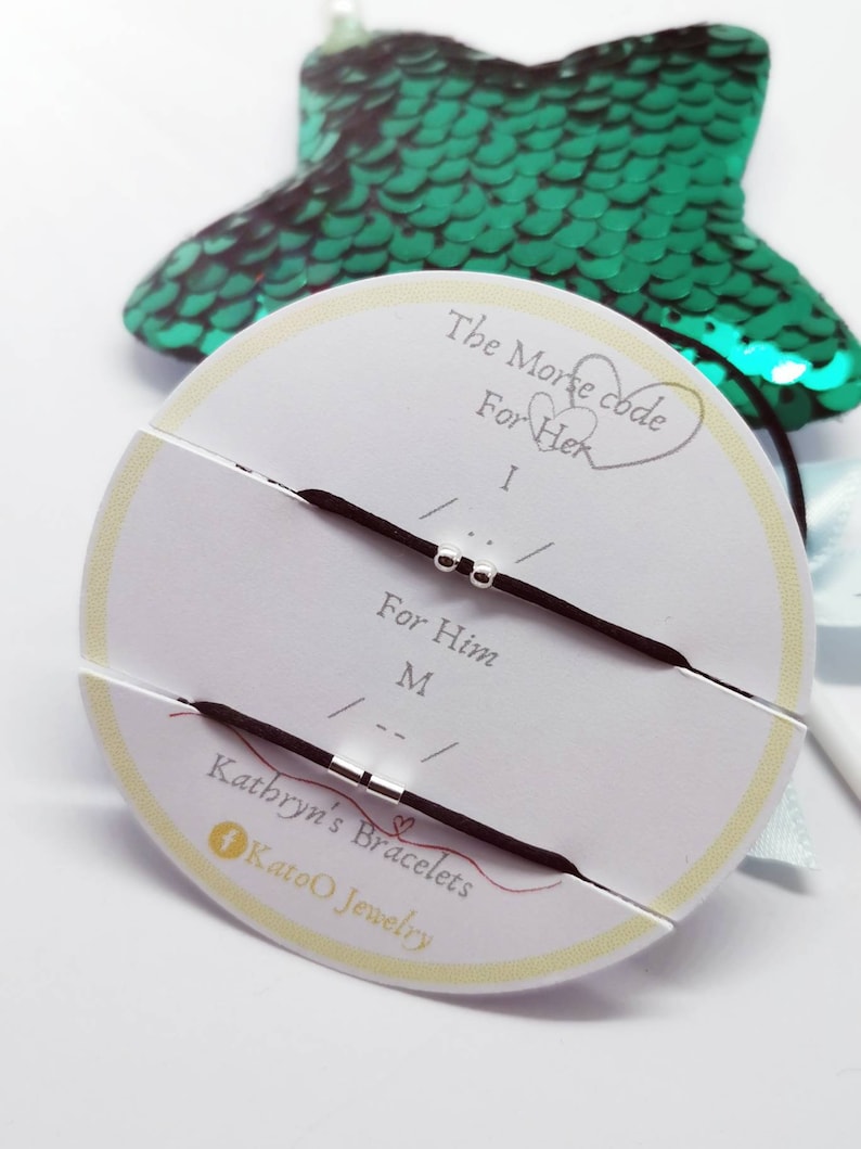 May include: Two black elastic bracelets with silver beads, displayed on a white circular card with the text "The Morse code For Her I ... For Him M ..." and "Kathryn's Bracelets KatoO Jewelry".