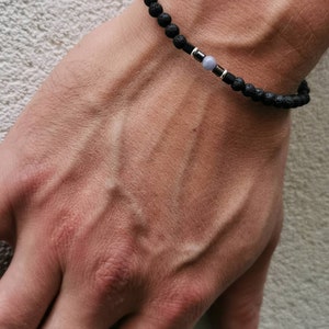 May include: A black lava rock beaded bracelet with a silver spacer and a light blue gemstone bead.