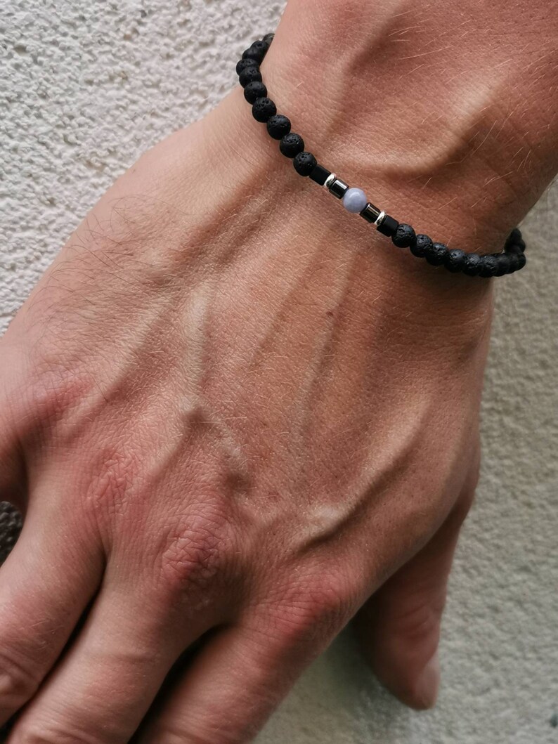 May include: A black lava rock beaded bracelet with a silver spacer and a light blue gemstone bead.