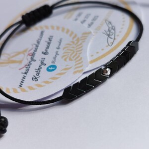 Puede incluir: Pulsera negra con un dije plateado y cuentas negras en forma de flecha. La pulsera está hecha con un cordón negro y tiene una cuenta de lava negra en el extremo.