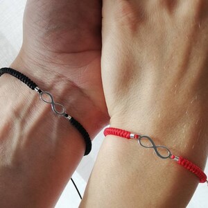 Puede incluir: Dos pulseras a juego, una negra y otra roja, cada una con un símbolo de infinito plateado. Las pulseras están hechas de cordón tejido y están diseñadas para usarse en la muñeca. Un diseño simple y elegante.