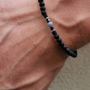 May include: A black lava rock bracelet with a silver bead and a light gray stone bead.