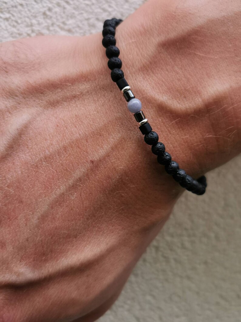 May include: A black lava rock bracelet with a silver bead and a light gray stone bead.