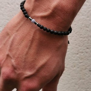 May include: A black lava rock bracelet with a silver bead and a light blue gemstone.