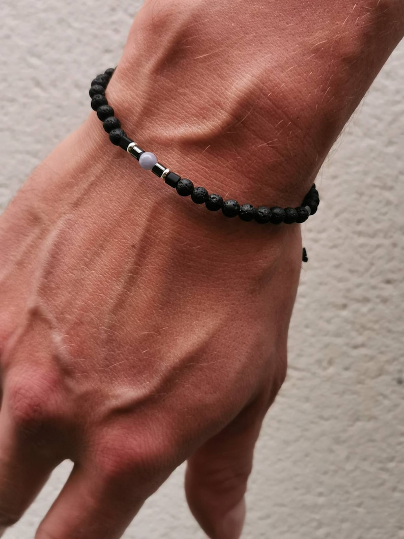 May include: A black lava rock bracelet with a silver bead and a light blue gemstone.