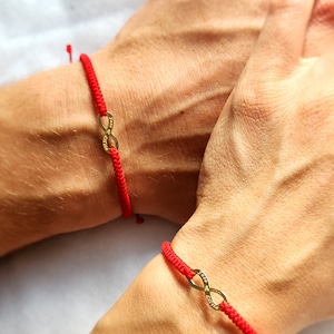 Puede incluir: Dos pulseras de cuerda roja con símbolos de infinito de oro. Los símbolos de infinito tienen las palabras "Forever" y "Always" grabadas.