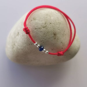 Könnte beinhalten: Ein rotes Armband mit einer silbernen Perle und einem dunkelblauen Edelstein.