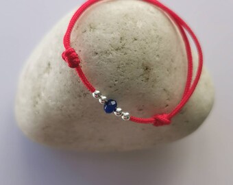 May include: A red string bracelet with a silver bead and a dark blue gemstone.