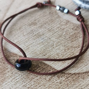 May include: A brown cord bracelet with a black bead and three silver metal beads.