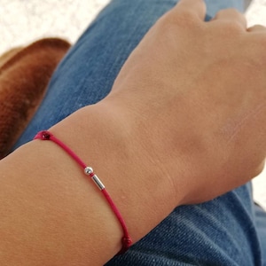 May include: A red string bracelet with a small silver bead and bar charm.
