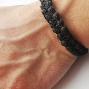 Puede incluir: Pulsera de roca volc&aacute;nica negra. La pulsera est&aacute; hecha de peque&ntilde;as cuentas de lava negra, redondas y porosas, ensartadas con un cord&oacute;n negro. La pulsera se lleva en la mu&ntilde;eca.