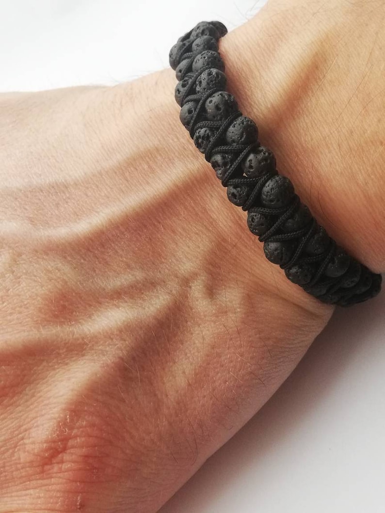 Puede incluir: Pulsera de roca volc&aacute;nica negra. La pulsera est&aacute; hecha de peque&ntilde;as cuentas de lava negra, redondas y porosas, ensartadas con un cord&oacute;n negro. La pulsera se lleva en la mu&ntilde;eca.