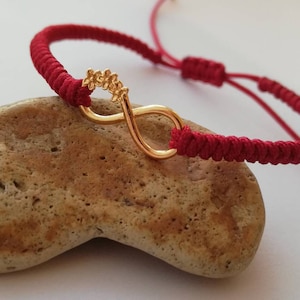 Puede incluir: Pulsera de cuerda roja con un dije de oro en forma de infinito. El dije está decorado con pequeñas cuentas doradas.