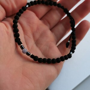 May include: A black lava rock beaded bracelet with a single light purple gemstone bead and silver accents.