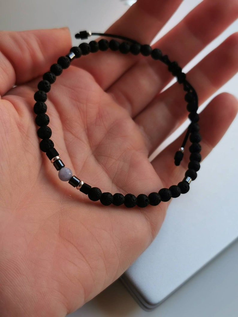 May include: A black lava rock beaded bracelet with a single light purple gemstone bead and silver accents.