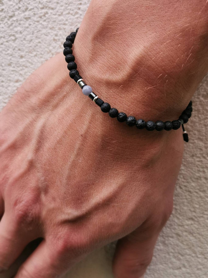 May include: A black lava rock bracelet with a silver bead and a gray stone bead.