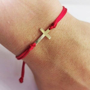 May include: A red string bracelet with a gold cross charm.