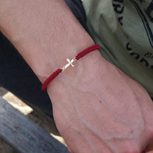 Könnte beinhalten: Ein rotes Armband mit einem kleinen goldenen Kreuzanhänger.