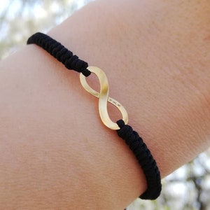 Puede incluir: Un brazalete de cordón negro con un dije de oro en forma de infinito. El dije está grabado con "AU 925 14K".