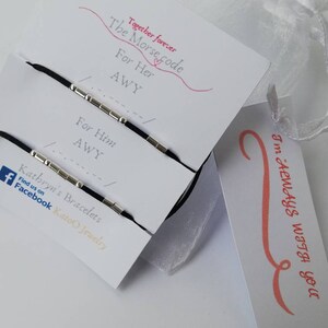 Pode incluir: Duas pulseiras de corda preta com contas prateadas que soletram "AWY" em código Morse. As pulseiras são embaladas em um cartão branco com o texto "Together forever The Morse code For Her AWY For Him AWY Kathryn's Bracelets Find us on Facebook Katoo Jewelry". Um cartão branco separado com um design de espiral rosa diz "I'm ALWAYS WITH YOU".