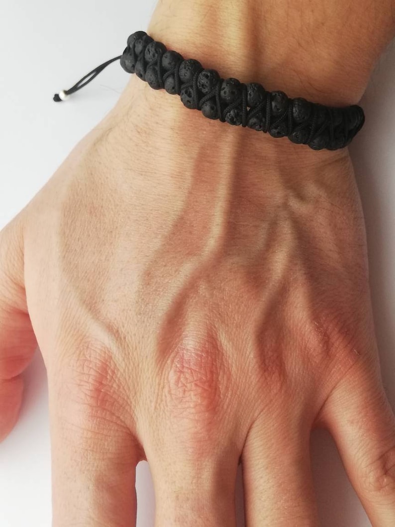 Puede incluir: Pulsera de roca volc&aacute;nica negra con cord&oacute;n negro ajustable. La pulsera presenta una doble hebra de cuentas porosas de color gris oscuro. El cord&oacute;n est&aacute; atado con una peque&ntilde;a cuenta blanca en el extremo. La pulsera se lleva en la mu&ntilde;eca.