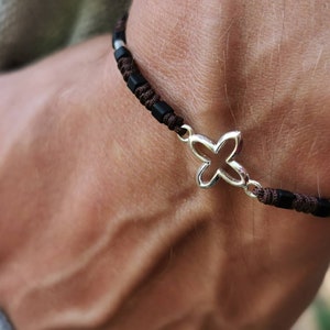 May include: A black and brown bracelet with a silver four-leaf clover charm. The bracelet is made of woven brown cord and black beads. The charm is a four-leaf clover design.
