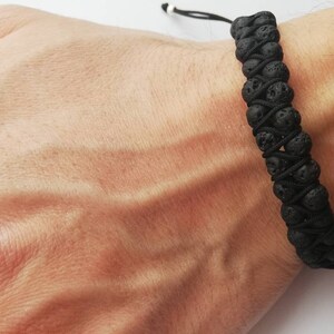 Puede incluir: Pulsera de piedra de lava negra. La pulsera presenta dos filas de cuentas de piedra de lava negra, conectadas por un cord&oacute;n negro. La pulsera es ajustable con un cierre de cord&oacute;n negro y blanco. La pulsera se lleva en la mu&ntilde;eca.
