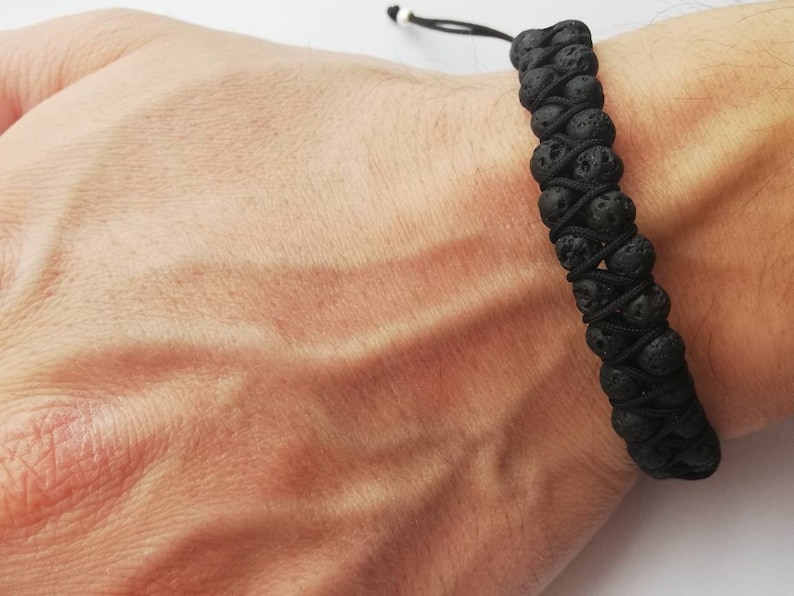 Puede incluir: Pulsera de piedra de lava negra. La pulsera presenta dos filas de cuentas de piedra de lava negra, conectadas por un cord&oacute;n negro. La pulsera es ajustable con un cierre de cord&oacute;n negro y blanco. La pulsera se lleva en la mu&ntilde;eca.