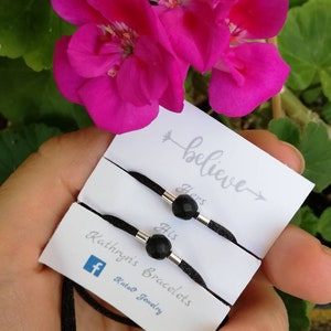 Puede incluir: Dos pulseras de cordón negro con cuentas de piedras preciosas negras y detalles plateados. Las pulseras están etiquetadas como "Suyo" y "Suya" y se empaquetan con una tarjeta que dice "Cree" y "Pulseras de Kathryn's".