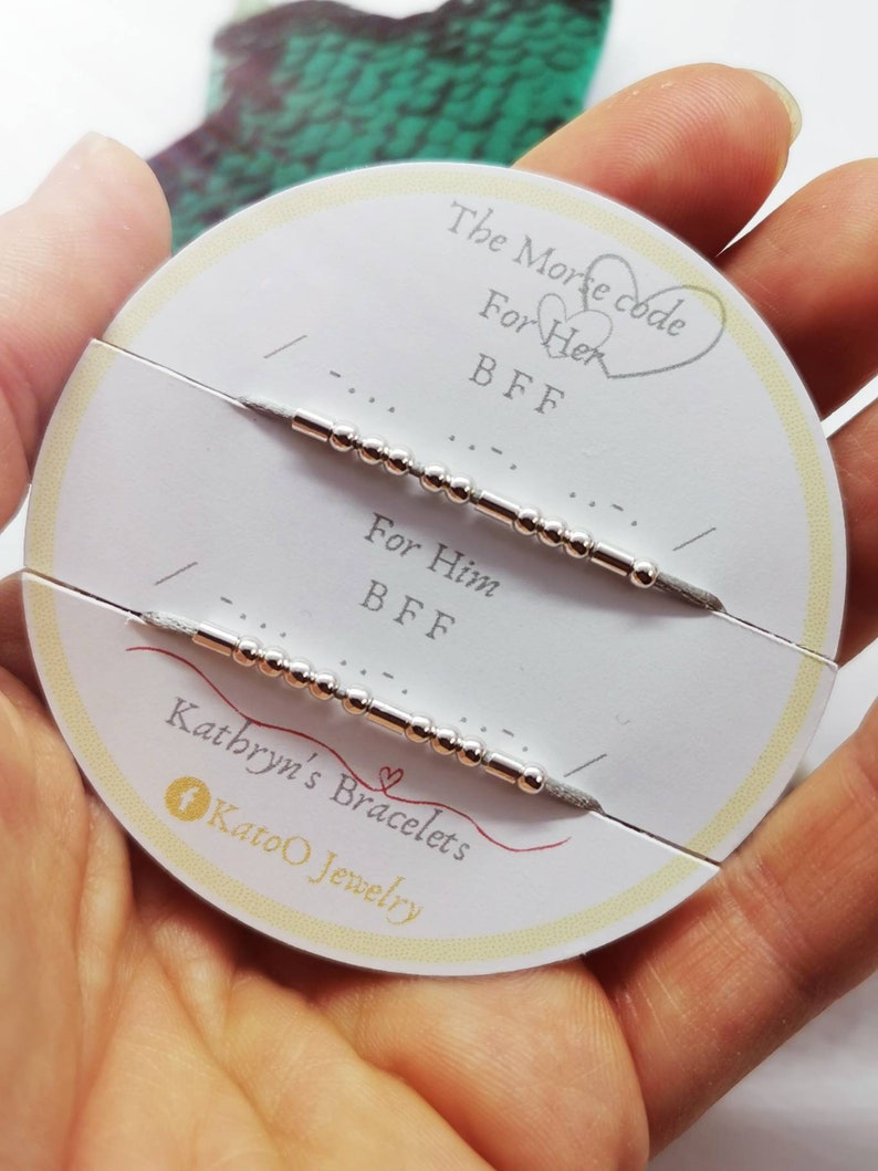 May include: A white card with the text "The Morse code" and two heart symbols. The card also has the text "For Her BFF" and "For Him BFF" with two silver bracelets with beads and a silver bar. The card also has the text "Kathryn's Bracelets Katoo Jewelry".