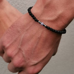 May include: A black beaded bracelet with a silver accent and a light blue gemstone.