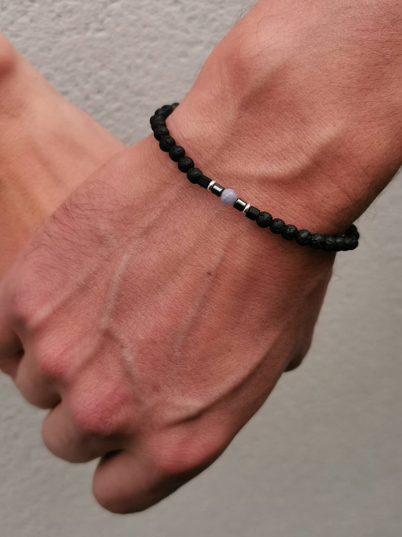 May include: A black beaded bracelet with a silver accent and a light blue gemstone.