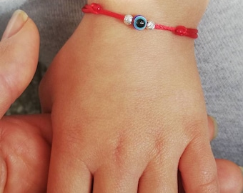 May include: A red string bracelet with a blue evil eye charm and silver beads.