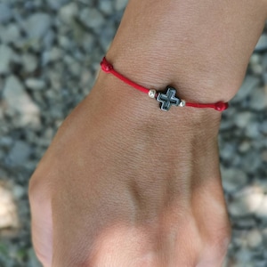 May include: A red string bracelet with a small silver cross charm.