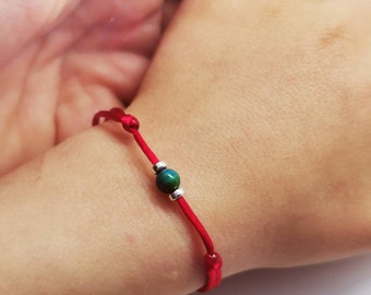 May include: A red string bracelet with a single green and silver bead.