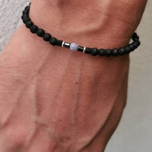 May include: A black lava rock bracelet with a single light blue gemstone bead and silver accents.